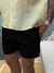 Homem usando shorts de linho preto ao lado de um barco, com camisa amarela e relógio prateado.