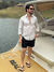 Homem sorridente usando shorts de linho preto e camisa clara, posando em um barco à beira de um lago.