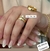 Par de alianças chanfradas douradas de 5mm com anel de diamante, exibidas em mãos com unhas decoradas.