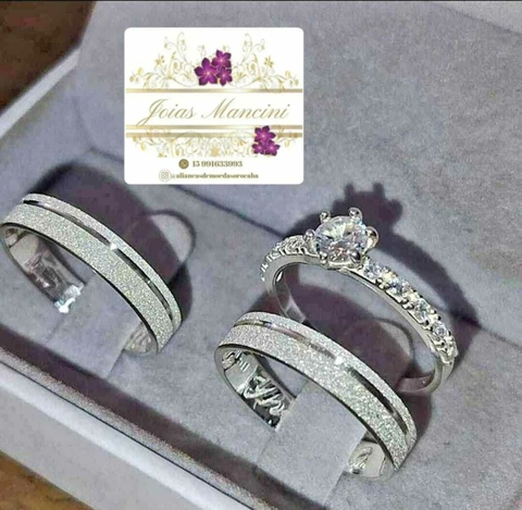 Par de alianças de namoro, com detalhes em prata e pedras brilhantes, apresentadas em uma caixa de joias. Modelo aliança com anel solitário modelo fininho fosqueado prata com anel prata pedras de zircónia