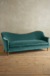 Sillón de dos cuerpos en un suave verde, con patas de madera, sobre un fondo claro y un piso de madera acogedor.