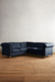 Sillón esquinero Chesterfield en color azul marino, con diseño acolchado y patas de madera en un ambiente minimalista.