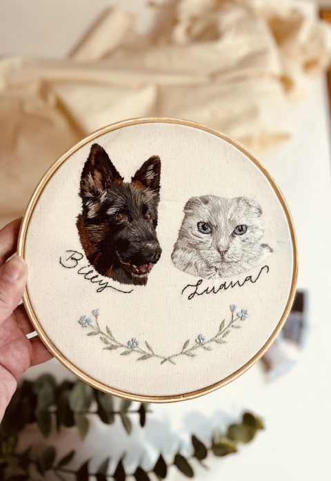 Retrato realista bordado à mão de dois gatos em bastidor de 20 cm, com nomes e ramos delicados.