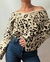 Polerón tejido con estampado animal print en tonos beige y negro, cuello amplio y hombros descubiertos, combinado con jeans azules