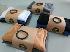 Conjunto de camisetas organizadas com faixas de papel kraft, cada uma acompanhada de uma pulseira.