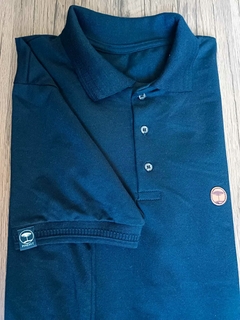 Camisa polo dobrada na cor azul escuro, com detalhes em botões e logotipo na manga.