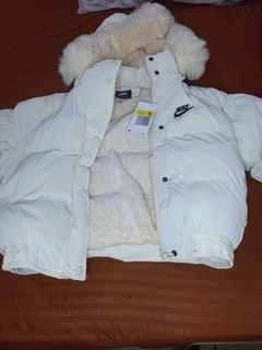 Campera puffer blanca de Nike, con capucha de pelaje y forro interior suave, sobre una superficie marrón.