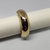 Elástico de metal dourado, com acabamento brilhante, posicionado sobre um suporte branco.