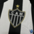 Camisa do Atlético Mineiro feminina, modelo Home 25/26, com listras pretas e brancas e detalhes em dourado.