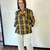 Mulher sorrindo usando um mini trench curto xadrez impermeável nas cores amarelo e preto, com calças brancas.