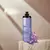 Frasco de desodorante corporal Nativa SPA Lilac, com flores roxas ao lado, em fundo neutro.