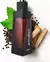 Frasco de perfume Coleção Malbec 100ml com fundo branco, rodeado por folhas verdes, grãos de pimenta e pedaços de madeira.