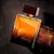 Frasco de perfume Natura Essencial 100ml com design moderno e cores quentes.