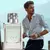 Frasco de perfume Zaad de 95ml ao lado de um homem elegante com camisa branca, segurando óculos de sol.
