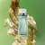 Frasco de perfume Natura Essencial Feminino de 100ml sobre fundo verde com flores ao redor.