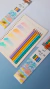 Lápis de cor de madeira em tons pastel organizados ao lado de um caderno com traços coloridos.