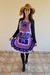 A mulher usa um avental junino caipira adulto, com estampas xadrez e detalhes em renda, posando alegremente com um chapéu de palha.