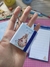 Chaveiro Post-it CapiMella em forma de bloco de notas, segurado por uma mão, com ilustração de uma capivara e flores.