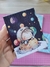 Porta bloquinho ilustrado com um astronauta feliz flutuando no espaço, cercado por planetas coloridos.
