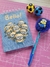 Caderneta A6 com tema dos Minions, caneta decorativa e duas bolinhas de futebol em um fundo rosa.