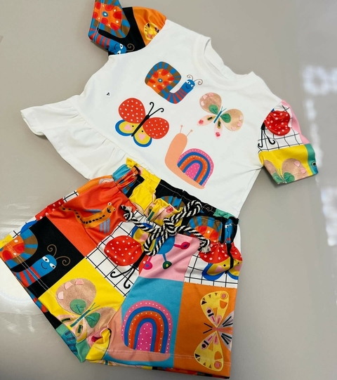 Conjuntinho infantil com estampa colorida de animais, incluindo uma camiseta branca com desenhos de insetos e um short com padrões vibrantes.