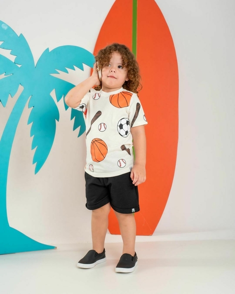 Criança com camiseta estampada de esportes e shorts pretos, posando ao lado de uma prancha de surf e palmeiras coloridas.