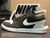 Imagem do modelo Jordan Low Linha Premium, destacando o design em preto e branco, com o logotipo da Nike ao fundo.