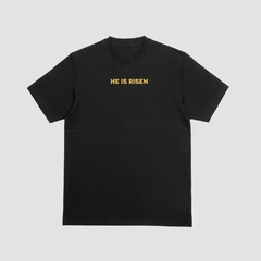 Camisa preta da Style fusion com a frase "HE IS RISEN" em destaque na parte frontal em amarelo.