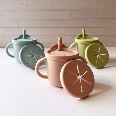 Vasos de silicón 3 en 1 de diferentes colores con tapa y popote, sobre una superficie blanca.