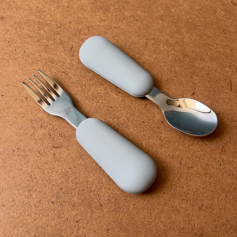 Cubiertos de acero inoxidable con mangos de silicón gris, incluyendo un tenedor y una cuchara.