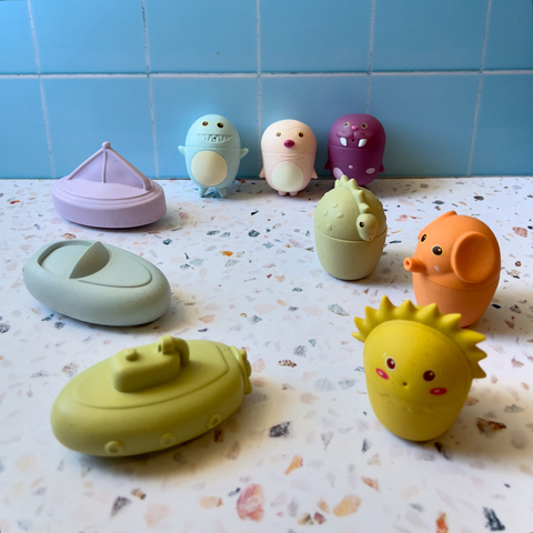 Conjunto de juguetes de baño para bebés que incluye varios personajes de colores y formas divertidas sobre una superficie clara.