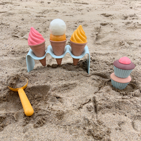 Set de juguetes de helados de playa en la arena, incluyendo conos y una cuchara de juguete.