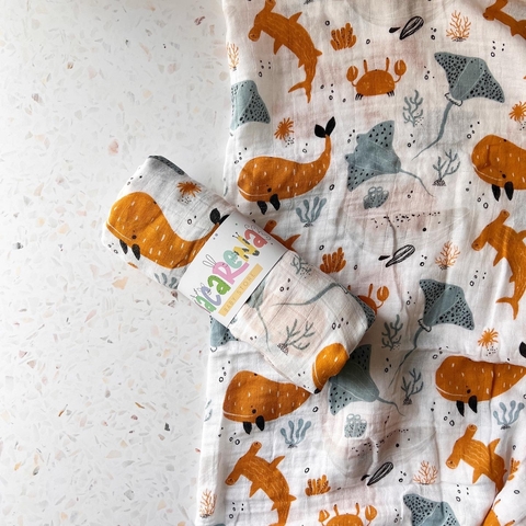 Muselina de algodón con estampado de animales marinos en colores naranja y azul, enrollada y con etiqueta.