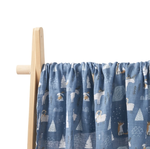 Muselina estampada en tonos azules con dibujos de alces, conejos y zorros, colgada en un soporte de madera.