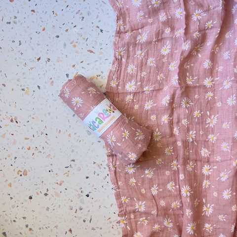 Muselina de color rosa con estampado de margaritas, enrollada y presentada sobre una superficie con textura.