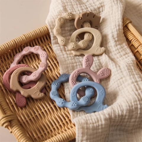 Mordederas de silicona en forma de conejo en tonos pastel, colocadas sobre una tela blanca y una cesta de mimbre.