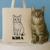 Tote bag personalizada color beige con dibujo de gato y el nombre junto a un gato real 