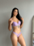 Modelo usando um conjunto de lingerie em renda lilás com bojo e aro, destacando detalhes delicados e um design elegante.
