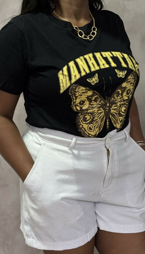 T-shirt preta com estampa de borboleta e texto "MANHATTAN", combinada com shorts brancos.