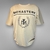 Camiseta Monastery en tono beige, perfecta para un estilo sobrio y sofisticado. Destaca por su diseño con la palabra "MONASTERY" en letras grandes y un escudo central con las iniciales "STM" enmarcadas por hojas de laurel, ofreciendo un look versátil y at