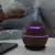 Umidificador de ar USB com luz roxa, em uma mesa ao lado de uma pessoa dormindo.