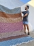 Homem segurando uma tapeçaria colorida, apresentando padrões distintos em tons de azul, vermelho, rosa e bege.