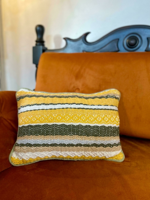 Almofada Colorétes em tons amarelo, verde e cinza, posicionada sobre um sofá laranja.