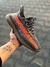 Tênis Adidas Yeezy Boost 350 V2 'Beluga' em uma mão, destacando seu design em tons de cinza e detalhes em laranja.