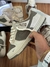 Tênis Nike Dunk Low x The North Face nas cores off white e cinza, sendo segurado por uma pessoa, com detalhes da embalagem e acessórios ao fundo.
