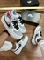 Tênis Nike Air Force 1 nas cores cinza e branco com detalhes em preto, posicionado sobre uma superfície de madeira com uma caixa ao fundo.
