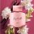 Perfume Impredecible para Mujer de Ésika, frasco de vidrio color rosa sobre fondo fuscia rodeado de flores.