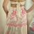 Vestido longo Laís na cor bege com detalhes em rosa, mostrando a parte de trás com laço nas costas e elástico  na cintura.