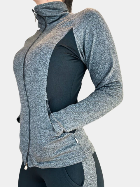 Foto da parte superior do corpo de uma mulher, de lado, vestindo uma jaqueta em action fleece thermo cinza mescla. A jaqueta possui gola alta, sem capuz, zíper frontal e bolsos laterais, bem como um recorte lateral na cor preta.