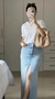 Mulher usando saia jeans longa com fenda na frente, camiseta branca e bolsa clara